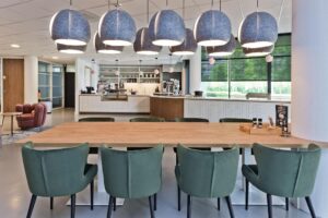 Moderne gemeenschappelijke keuken en zithoek met houten tafel, groene stoelen en grote grijze hanglampen aan de Prof. W.H. Keesomlaan.
